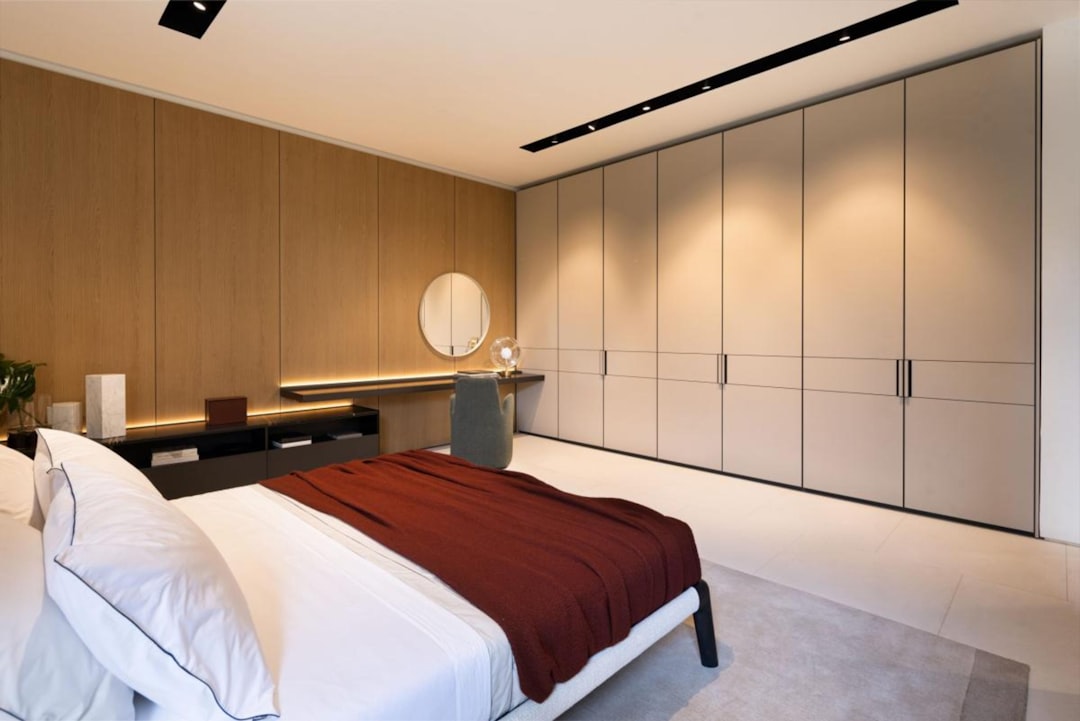 services-01 A serene and minimalist bedroom with Poliform furniture, showcasing a sleek bed, modern wardrobe, and a stylish vanity area. The warm wood tones and soft lighting create a cozy, refined atmosphere, perfect for modern living spaces.