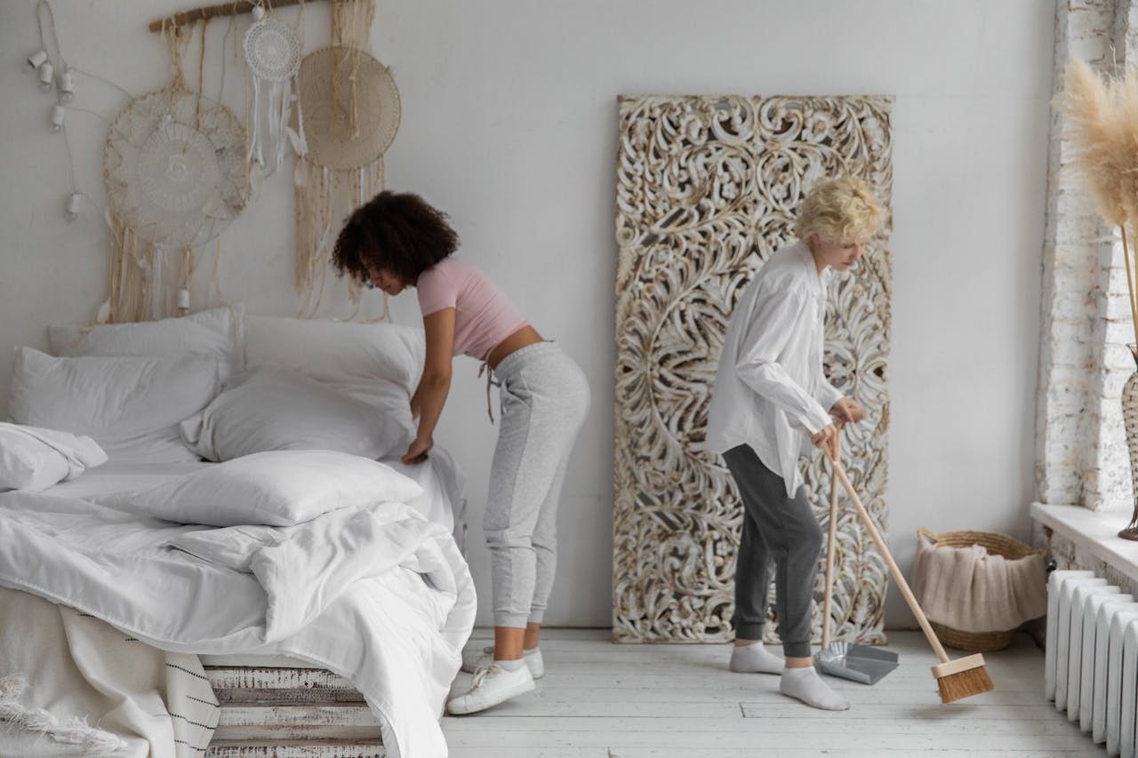 about-01 Two women tidying a contemporary bedroom with natural decor elements, showcasing stylish cleaning habits.
